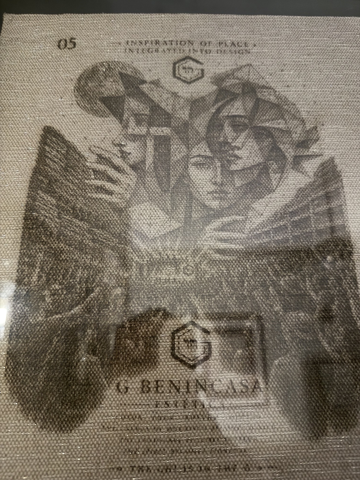 Faceted winged-face artwork on a coarse woven textile surface.